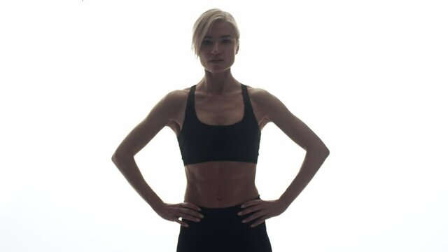 Woman of athletic build stands on white background with hands on hips, front view. Woman with developed muscles stands in studio in sports uniform
