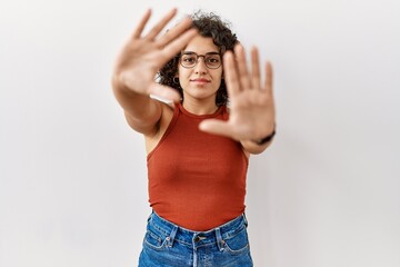 Young hispanic woman wearing glasses standing over isolated background doing frame using hands palms and fingers, camera perspective
