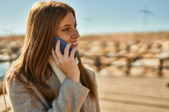 Young redhead girl smiling happy talking on the smartphone at the beach.