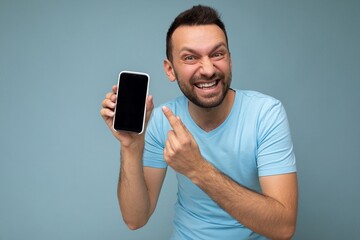 Photo of handsome crazy emotional smiling adult male person good looking wearing casual outfit standing isolated on background with copy space holding smartphone showing phone in hand with empty