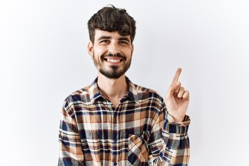 Fototapeta premium Hispanic man with beard standing over isolated background with a big smile on face, pointing with hand and finger to the side looking at the camera.