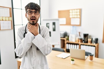 Hispanic man with beard wearing doctor uniform and stethoscope at the office shouting and suffocate because painful strangle. health problem. asphyxiate and suicide concept.