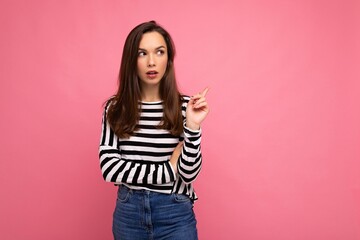 Shot of young positive happy thoughtful attractive brunette woman with sincere emotions wearing casual striped longsleeve isolated on pink background with empty space and thinking