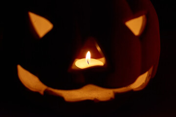 A glowing carved pumpkin with a candle inside in a dark background - halloween concept