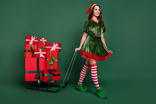 Full size profile side photo of young girl happy smile go sledge present box santa helper isolated over green color background