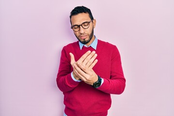 Hispanic man with beard wearing business shirt and glasses suffering pain on hands and fingers,...