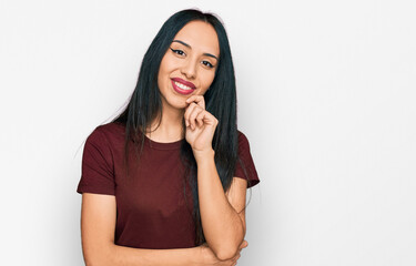 Fototapeta premium Young hispanic girl wearing casual t shirt looking confident at the camera with smile with crossed arms and hand raised on chin. thinking positive.