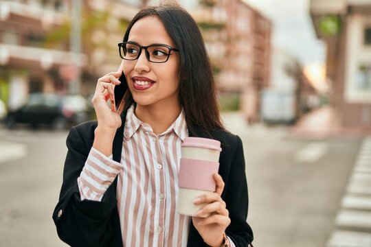 Young hispanic businesswoman talking on the smartphone and drinking coffee at the city.