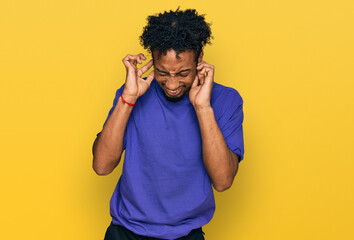 Young african american man with beard wearing casual purple t shirt covering ears with fingers with annoyed expression for the noise of loud music. deaf concept.