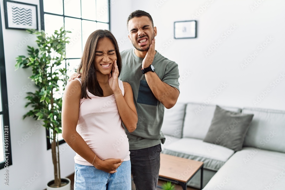 Poster Young interracial couple expecting a baby, touching pregnant belly touching mouth with hand with painful expression because of toothache or dental illness on teeth. dentist concept.