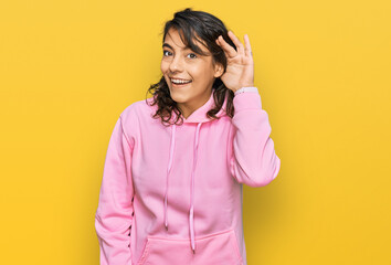 Young hispanic woman wearing casual sweatshirt smiling with hand over ear listening an hearing to rumor or gossip. deafness concept.