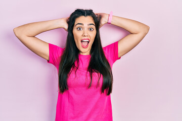 Fototapeta na wymiar Young hispanic girl wearing casual pink t shirt crazy and scared with hands on head, afraid and surprised of shock with open mouth