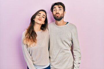 Young hispanic couple wearing casual clothes looking at the camera blowing a kiss on air being lovely and sexy. love expression.