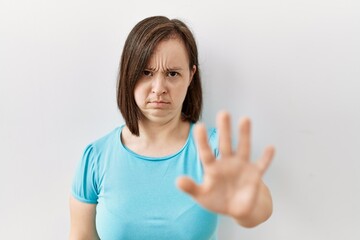 Young down syndrome woman standing over isolated background doing stop sing with palm of the hand. warning expression with negative and serious gesture on the face.