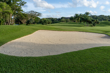 The golf course sand obstacles have clear skies and beautiful natural trees