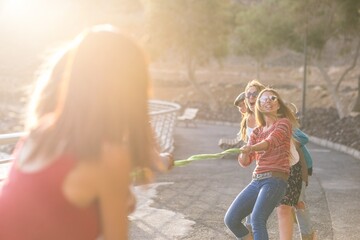 Group of female friends playing tug of war with rope at garden. Women enjoying summer holidays...