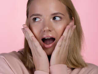 cute young blonde in a pink hoodie is shocked and surprised, says wow.