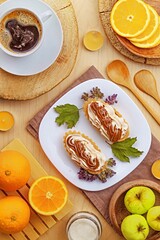 There are two cream cakes on a white dessert plate, and next to them are fruits and black coffee
