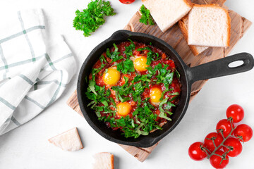 Shakshouka with quail eggs and tomato sauce topped with herbs served in cast iron pan. Middle Eastern and African meal. Top view