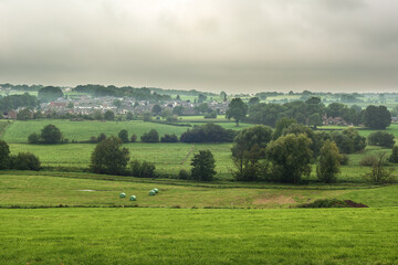 Valley with meadows, trees and a small village in a hilly landscape under a cloudy sky.