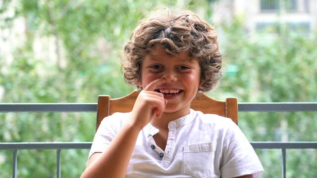 Funny 7-year-old boy picks his nose - childlike behavior typical of children - put finger in nose sign of rudeness