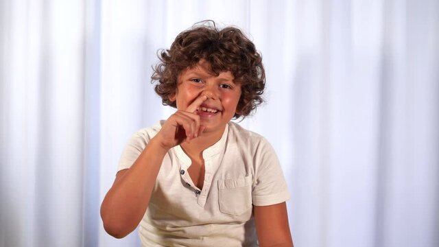 Funny 7-year-old boy picks his nose - childlike behavior typical of children - put finger in nose sign of rudeness