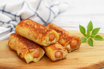 Delicious homemade fried or baked rolls made of wheat bread, sausage and cheese. Gourmet breakfast, brunch. Served on a wooden board with basil. White background. Selective focus, copy space
