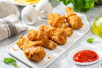 Fried crispy chicken legs in breadcrumbs on a white ceramic serving board on a light culinary background. Fast food from the drumstick close-up
