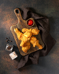 Fried crispy chicken legs in breadcrumbs on a wooden serving board on a dark background. Fast food from the drumstick top view
