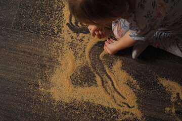 Dziecko rysuję po rozsypanej krupie na podłodze - obrazy, fototapety, plakaty