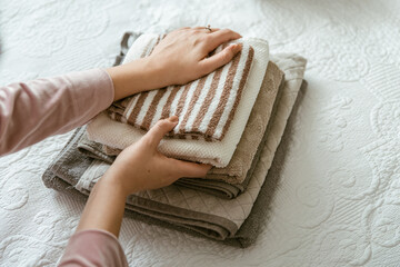 Woman folding laundry and towels in bedroom, organizing clothes in wardrobe. Concept of minimalist...