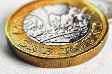 The British 1 pound sterling coin is lying on a white surface. Not isolated. Economy, money and banking in England. Focus is on the inscription with nominal value and name of the UK currency. Macro