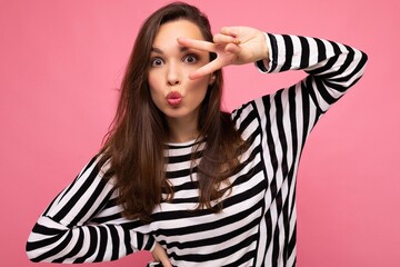 Photo of young european positive winsome happy beautiful brunette woman with sincere emotions wearing stylish striped longsleeve isolated on pink background with copy space