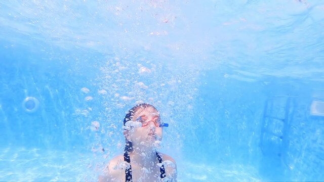 Underwater bubbles slowly rise to water surface from girl swimming in hotel pool