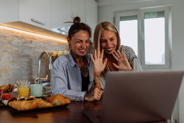 Lesbian couple in pajamas having video call in the kitchen