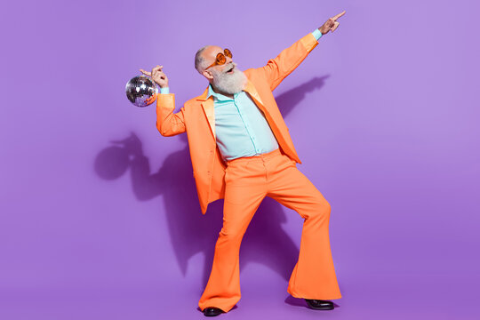 Full length photo of old positive happy man hold disco ball point look empty space isolated on purple color background
