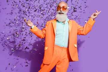 Photo of cheerful positive old man look empty space confetti fall smile isolated on purple color...
