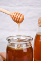 honey in glass jar and dripping from wooden dipper, on white background