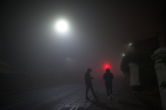 Hooded youths loiter on a dim street corner using mobile smartphones.