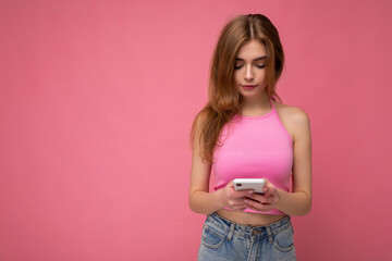 Beautiful young woman wearing casual clothes standing isolated over background surfing on the internet via phone looking at mobile screen