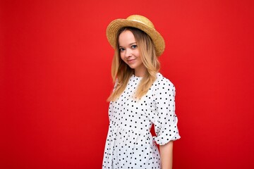 Photo shot of young beautiful cute happy blonde woman wearing casual dress and straw hat isolated over red background with copy space