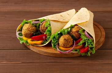 Tortillas wrapped with falafel balls and fresh vegetables, vegetarian healthy food, on a wooden...