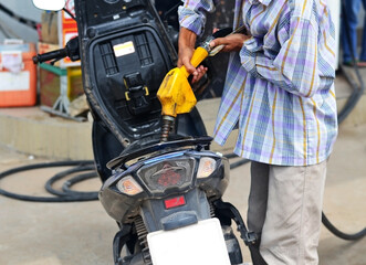 Fototapeta na wymiar A man in a plaid shirt refueling a motorbike at a gas station