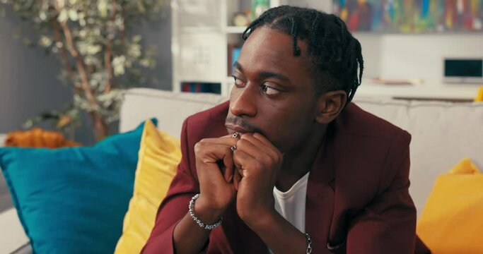 Dark skinned man with dreadlocked wearing smart suit sitting in office hands resting on knees joined in front of face worry sadness pondering company problems money troubles thinking of solution