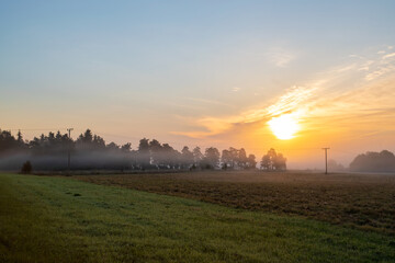 Obraz na płótnie Canvas Sunrise over the meadow. Early autumn morning in the countryside. Light shining in the morning foggy field.