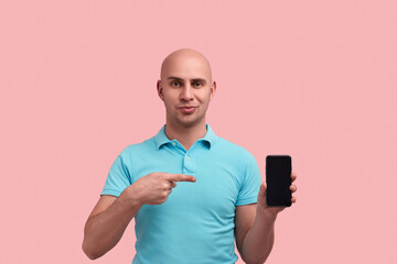 Handsome bald unshaven homosexual man demonstrates smartphone screen, indicates deal or product...