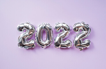 Banner. Happy New Year's Holiday. Balloons made of silver foil with the number 2022 and silver confetti on a fashionable purple background. Flat lay.
