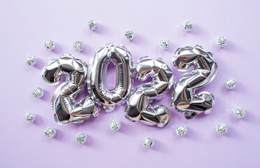 Banner. Happy New Year's Holiday. Balloons made of silver foil with the number 2022 and silver confetti on a fashionable purple background. Flat lay.