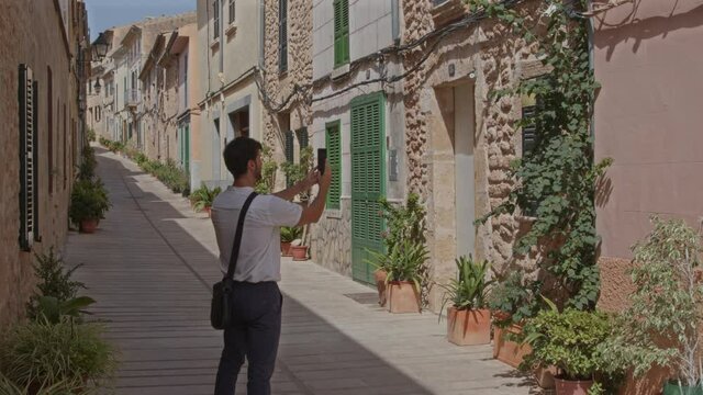 Hombre se hace un selfie con el m&oacute;vil en calle con casas estilo mediterr&aacute;neo  (Grabado en 6K con blackmagic RAW)