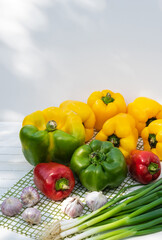 Red, yellow-green ripe bell peppers, green onions and garlic, autumn harvest on wooden background, selective focus
